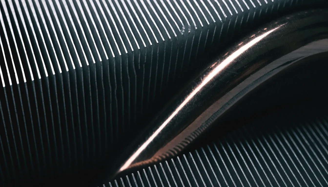 Raking macro photograph across an aluminium cooler fin stack and a copper heatpipe bend